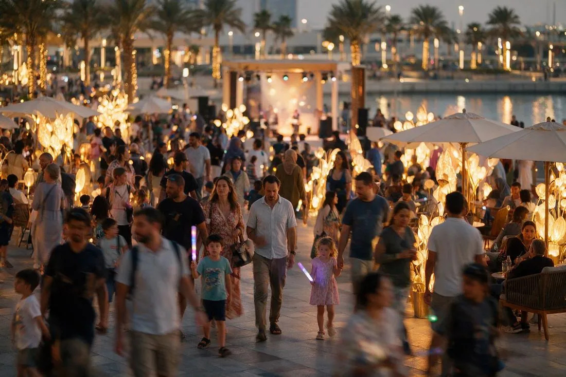Crowds at an evening outdoor festival lit with string lights and palm trees